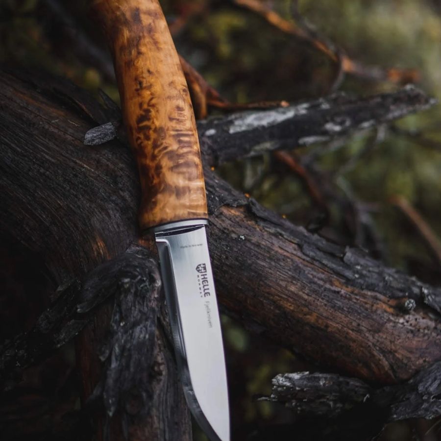Helle Fjellkniven 12C27 bushcraft knife resting on a moss-covered log in a forest, highlighting its natural wood handle and sharp Scandinavian blade.
