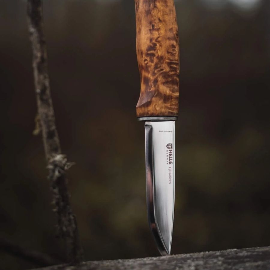 Helle Fjellkniven 12C27 bushcraft knife resting on a moss-covered log in a forest, highlighting its natural wood handle and sharp Scandinavian blade.