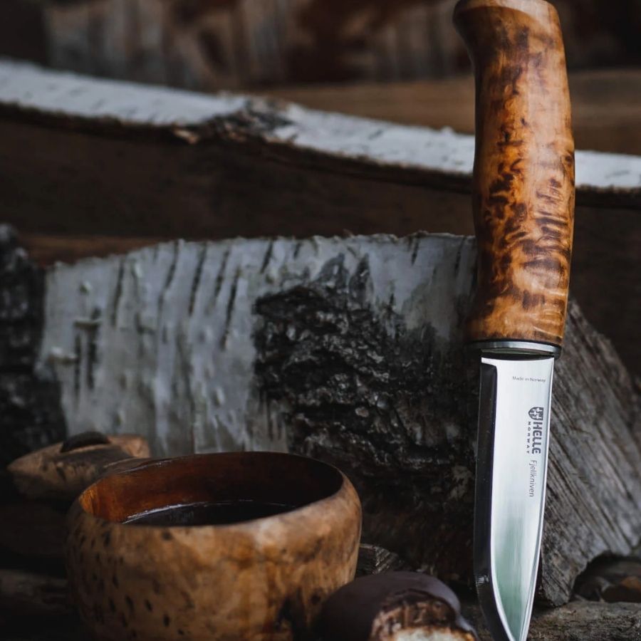 Helle Fjellkniven 12C27 bushcraft knife resting on a moss-covered log in a forest, highlighting its natural wood handle and sharp Scandinavian blade.